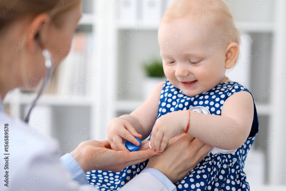 Pediatrician is taking care of baby in hospital. Little girl is being examine by doctor with stethoscope