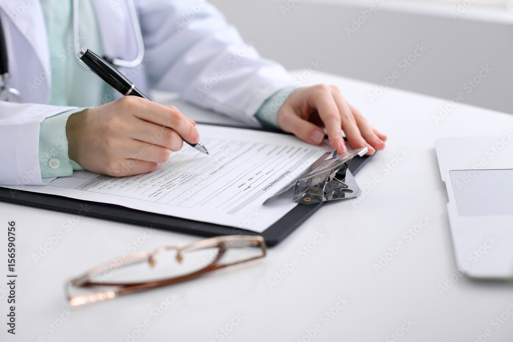 Close-up of a female doctor filling  out application form , sitting at the table in the hospital