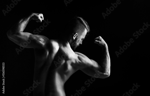 The back view torso of attractive male body builder on black background.