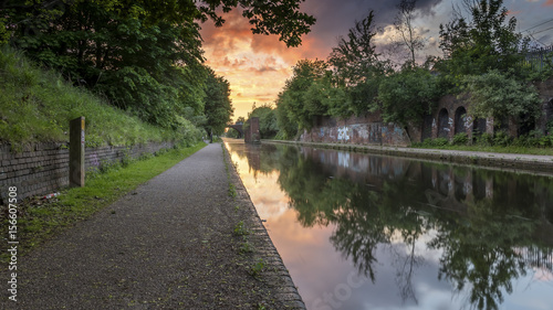 Sunset over the canal in Birmingham, UK, on a deserted footpath, with foliage flanking the tow path.  The sun is creating a dramatic red and orange cloudscape in the sky photo