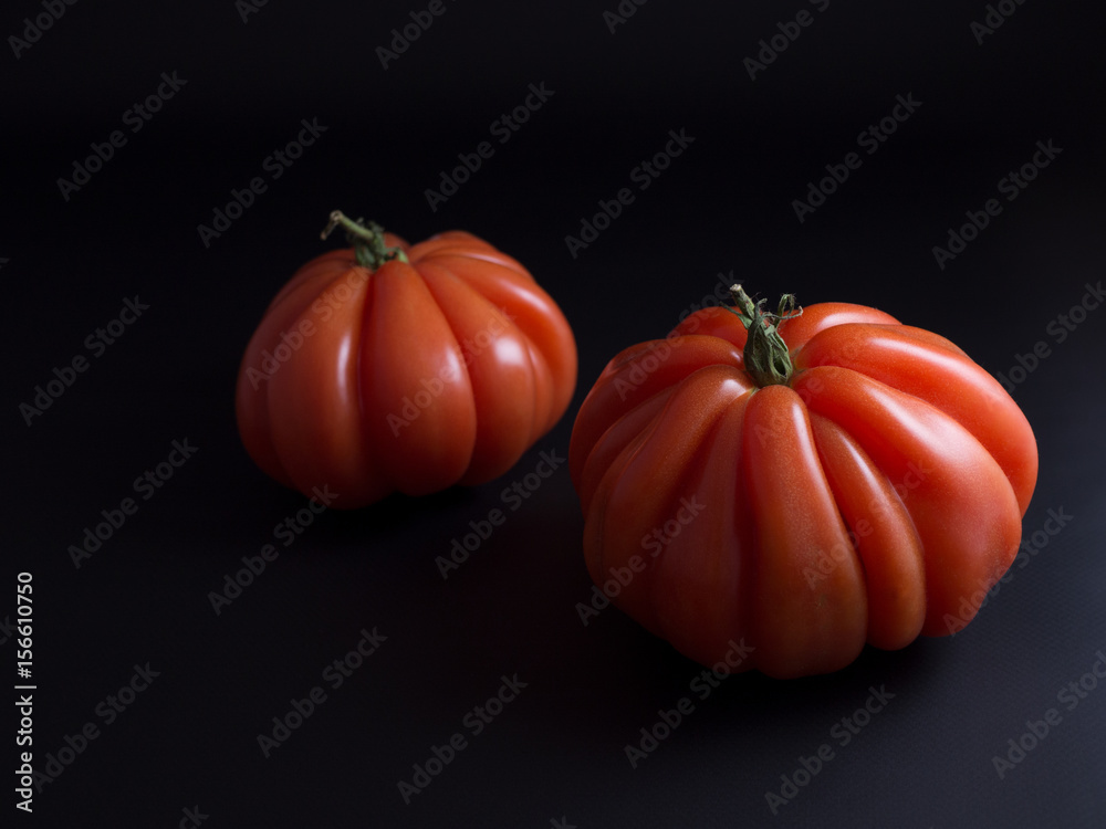 Two red beef tomatoes with green stems isolated on black background