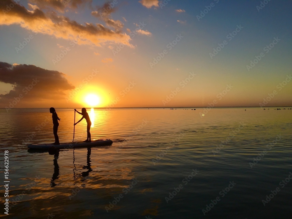 Two little girls do stand up paddling in the lagoon of Moorea during sunset, Moorea, Tahiti, French Polynesia