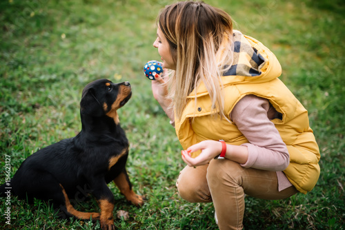 Cheerful pretty young woman sitting and playing fetch with her dog on grass.