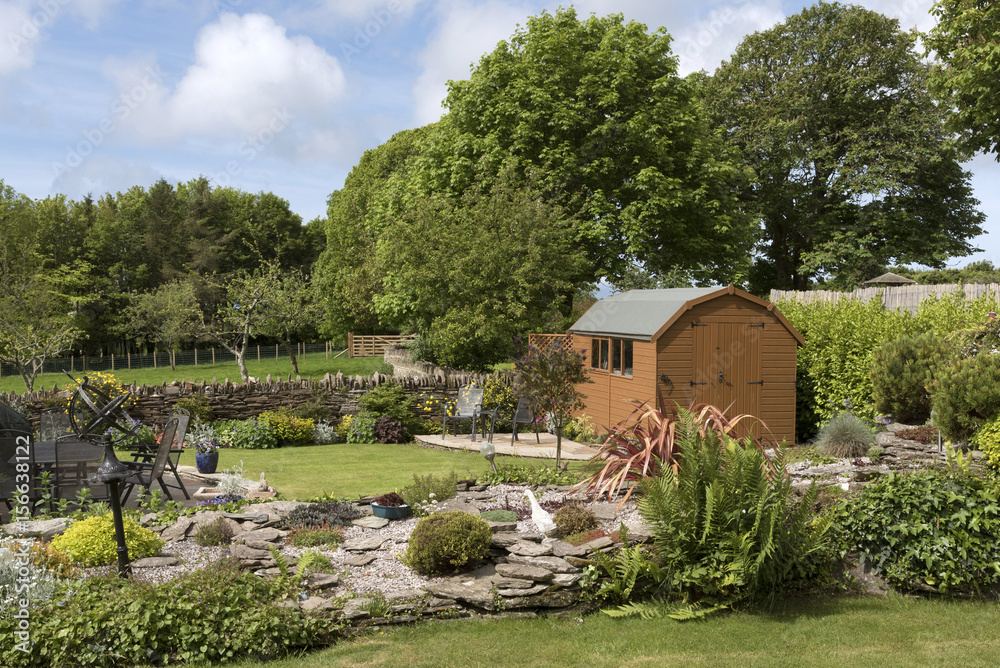 A Dutch barn style garden shed with a patio in a English country garden A Dutch barn style garden shed with a patio in a English country garden
