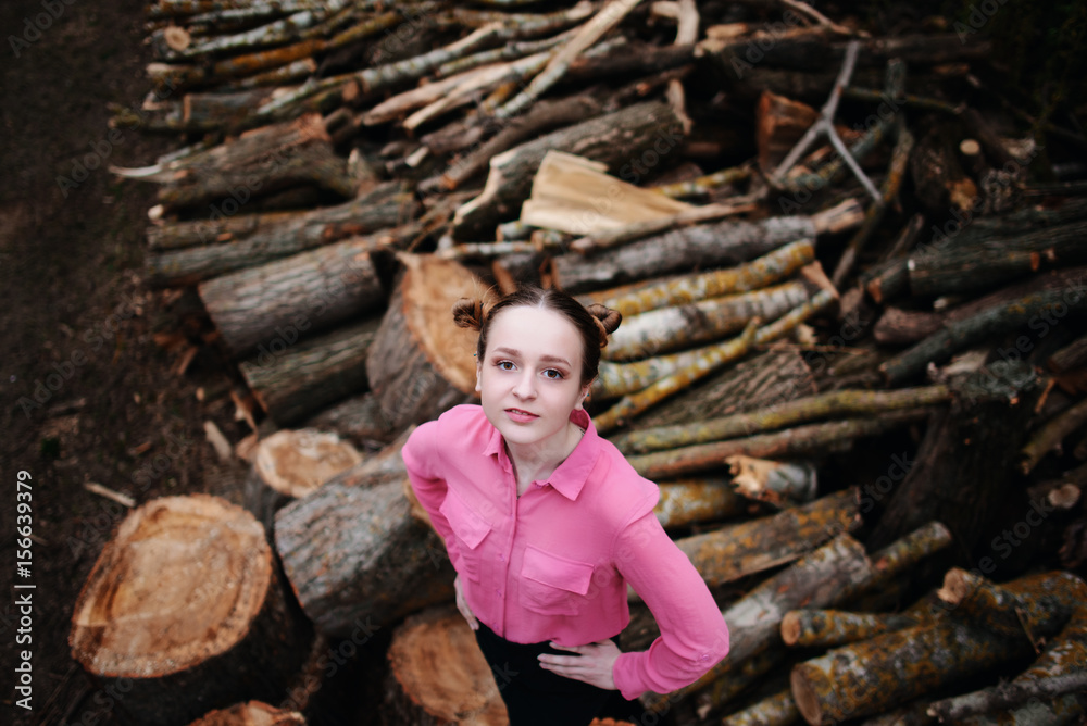 Beautiful young woman standing and looking at the camera on stack of felled tree trunks in the forest