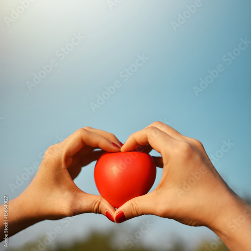 Red nails hand of hipster woman raising and hold a red heart up into sky, love and care concept