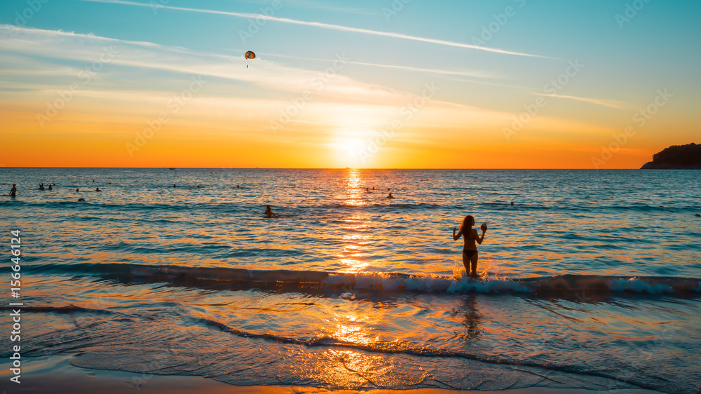 Sunset on a tropical beach. The picture aspect ratio is 16:9. The face and figure of the girl are changed 