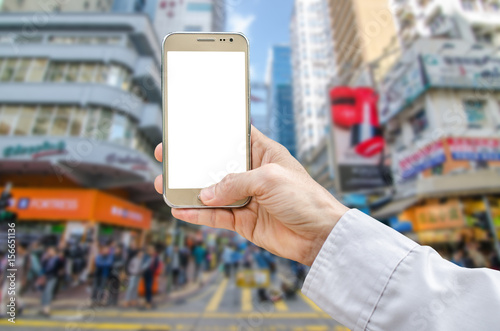 Mockup image of hand holding gold mobile phone with blank white screen and blurred city in the background