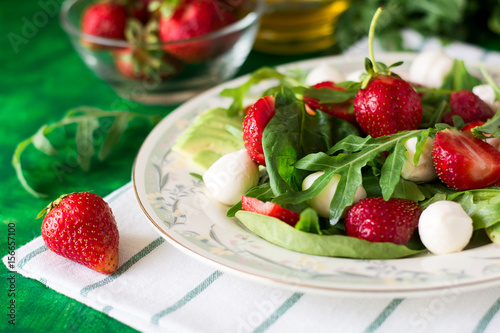 Fresh vegetarian salad with spinach  arugula  avocado slices  strawberries and mini mozzarella on green wooden table. Selective focus