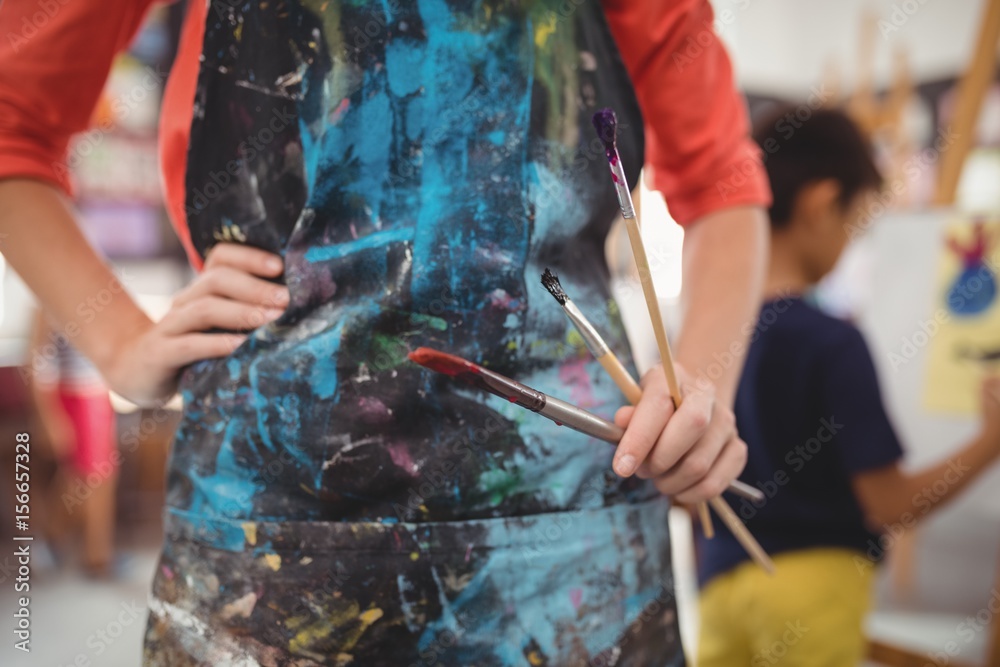Fototapeta premium Mid section of teacher standing with paintbrushes