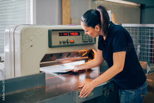 Worker in printing centar uses paper guillotine machine knife photo