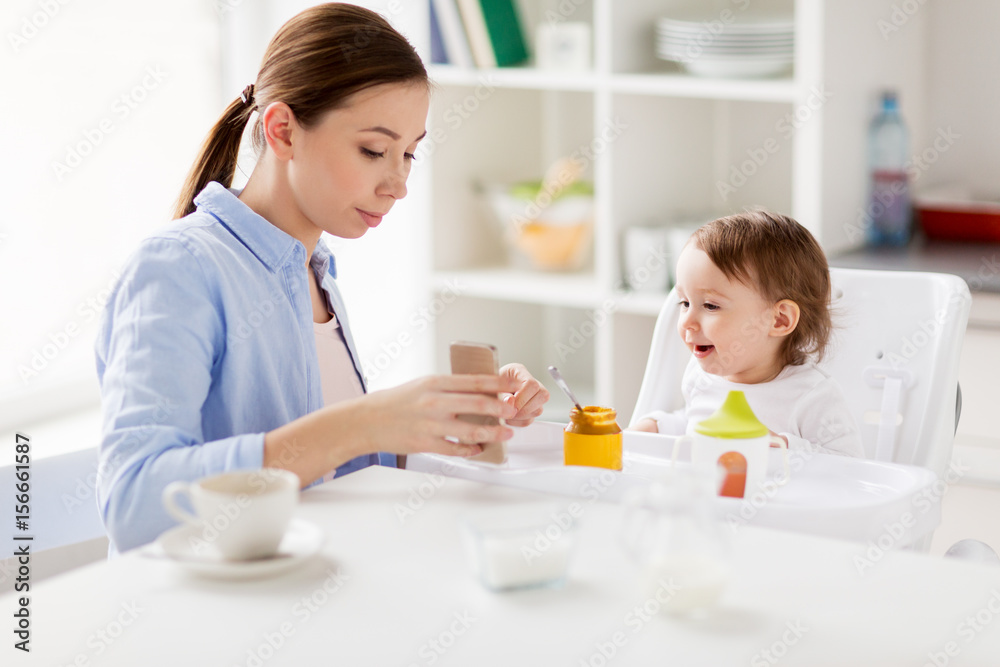 mother with smartphone and baby eating at home 