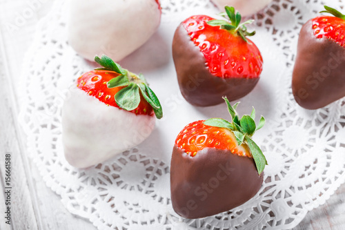 Fresh strawberries dipped in dark and white chocolate on light background close up. Delicious dessert and candy