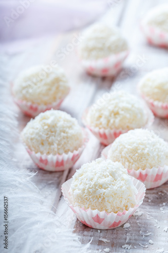 Homemade white truffles candy dessert sprinkled in coconut chips on wooden background close up. Delicious chocolate praline