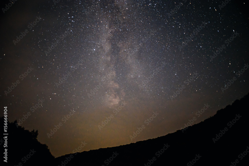 A clear night sky with a hill and trees in the foreground A clear night sky with a hill and trees in the foreground