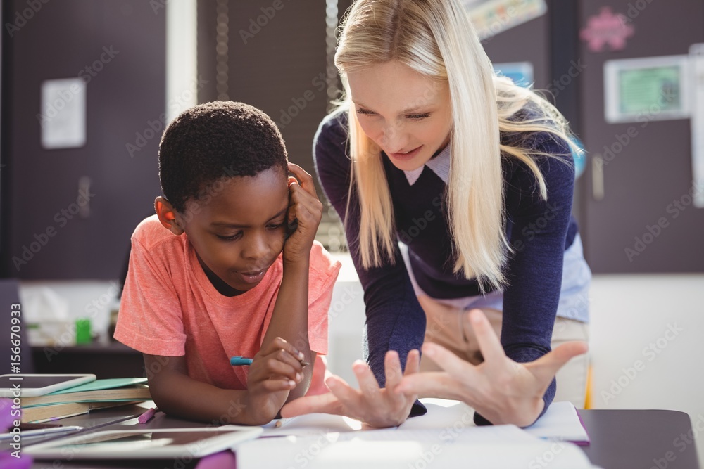 Teacher helping schoolgirl with her homework in classroom Teacher helping schoolgirl with her homework in classroom