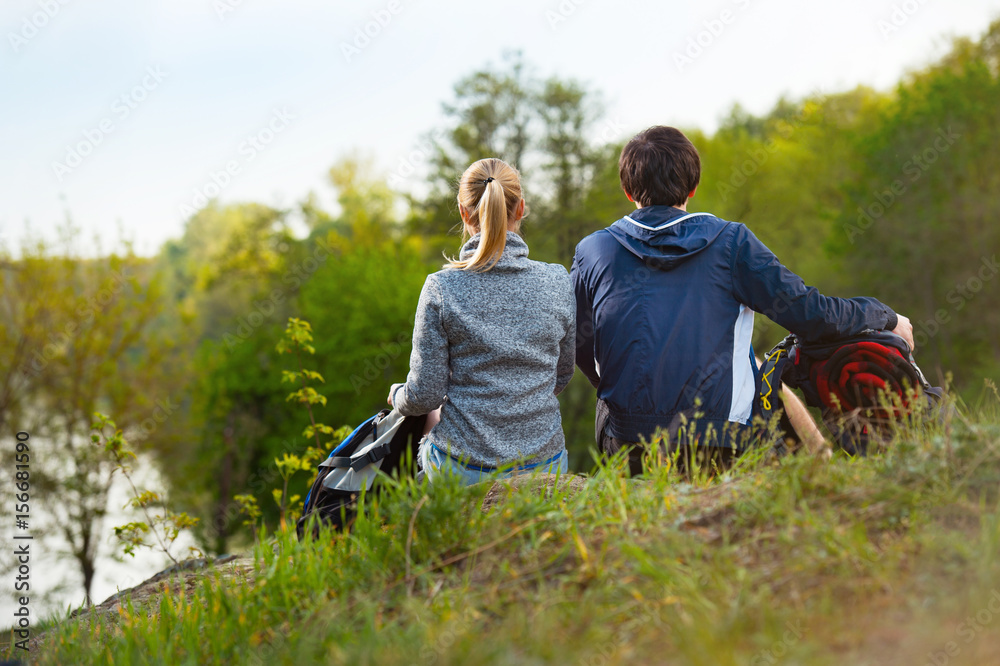 couple of hikers with backpacks looking at a beautiful river and forest. Back view. Travel, vacation, holidays and adventure concept. couple of hikers with backpacks looking at a beautiful river and forest. Back view. Travel, vacation, holidays and adventure concept.