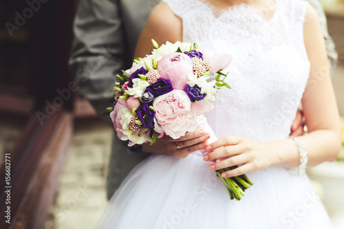 Hands of the newlyweds with a bouquet of the bride close-up. Marriage concept.
