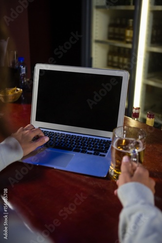 Mid-section man having beer while using laptop at counter
