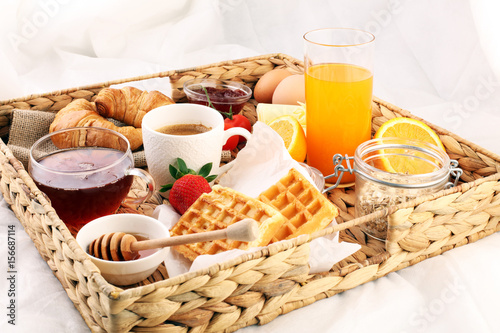 breakfast in bed with fruits and pastries on a tray -waffles, croissants, coffe and juice