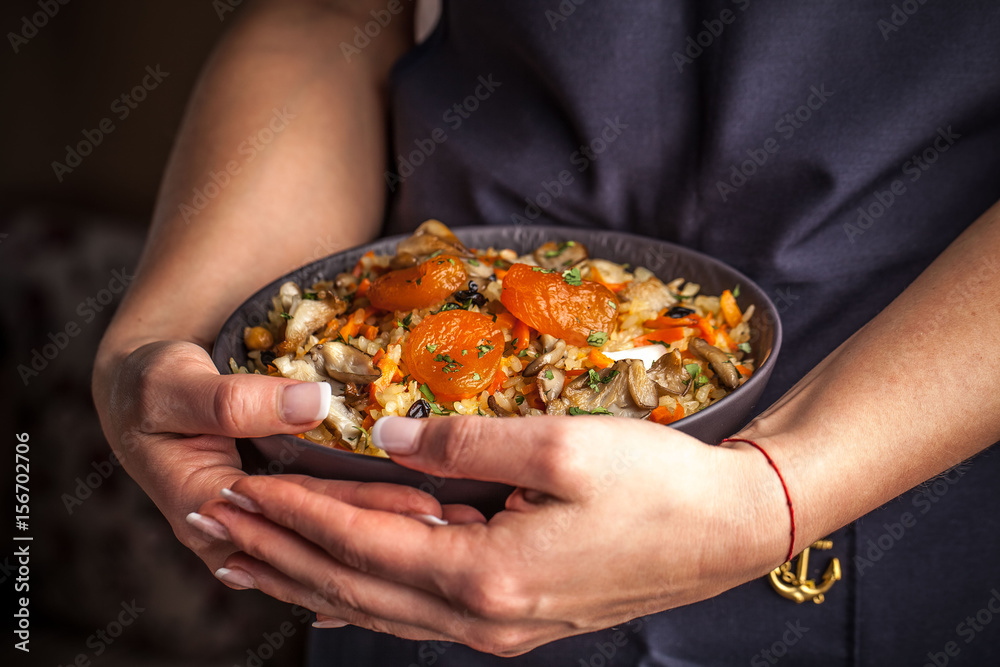 The girl cook holds a plate with a vegetarian plov, Uzbek traditional cuisine