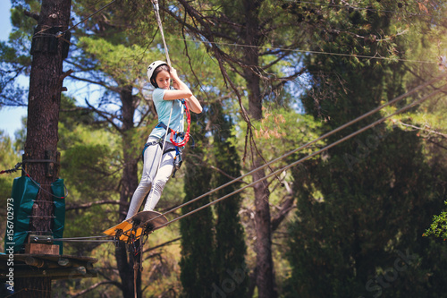 Happy school girl enjoying activity in a climbing adventure park on a summer day