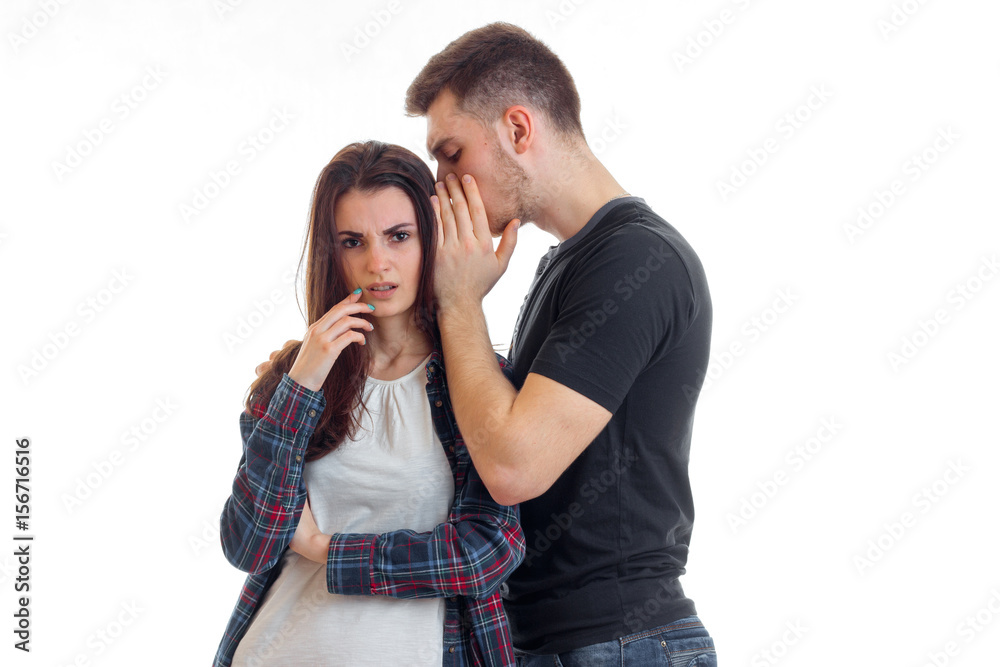 a young thoughtful girl standing next to a guy that whispers in her ear words close-up
