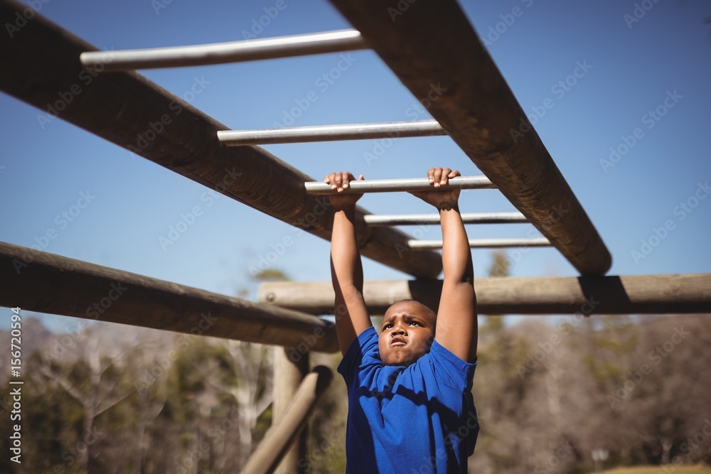 Fototapeta premium Determined boy exercising on monkey bar during obstacle course