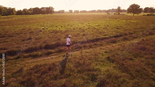 Wallpaper Mural A man runs in the countryside at sunset. Back view, young caucasian male, white t-shirt, summer season. 4K UHD graded file, follow aerial shot. Torontodigital.ca
