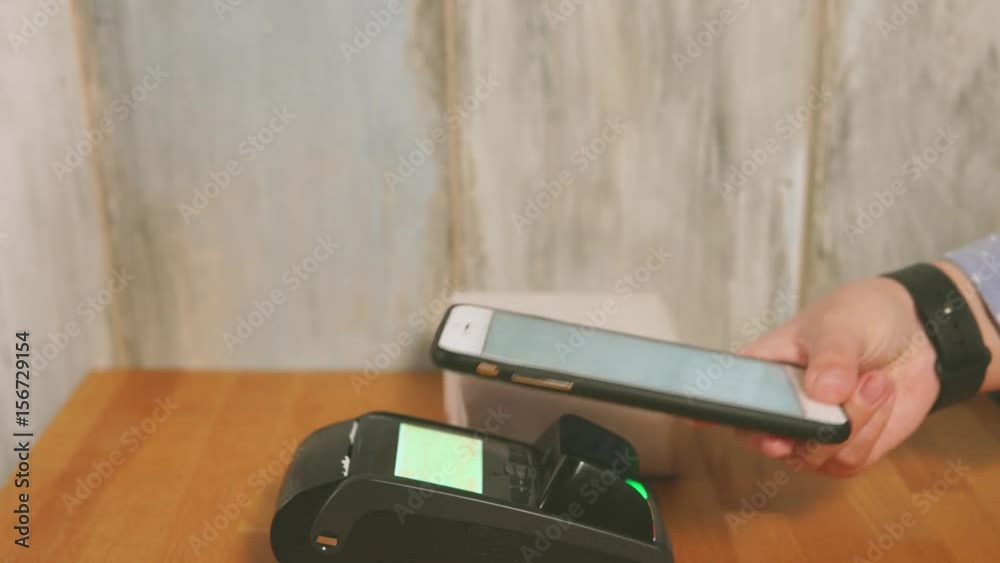 Close up view process of contactless payment. Seller put the payment terminal on the table and customer paying a bill by contactless method with his smartphone. Close up view process of contactless payment. Seller put the payment terminal on the table and customer paying a bill by contactless method with his smartphone.