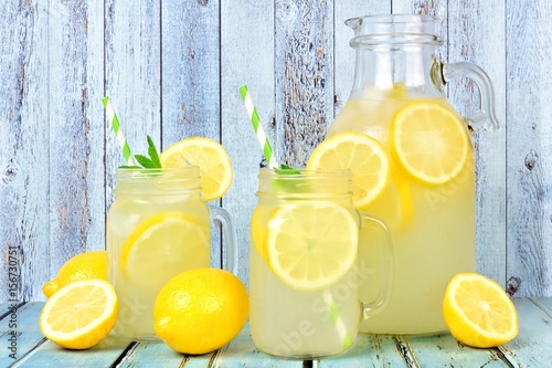 Vintage pitcher of lemonade with two mason jar glasses and lemons on rustic blue wood background photo