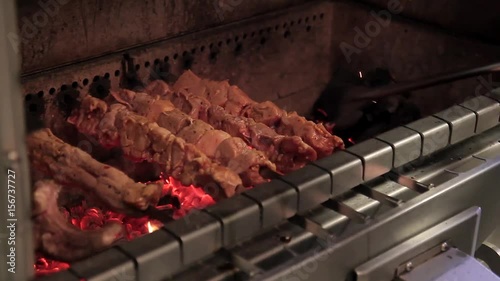 The chef roasts grilled various kinds of meat over charcoals in the restaurant. The cook stokes the fire with poker and shove live coals aside. Pieces of meat, kebab, and rib with spice are skewered photo