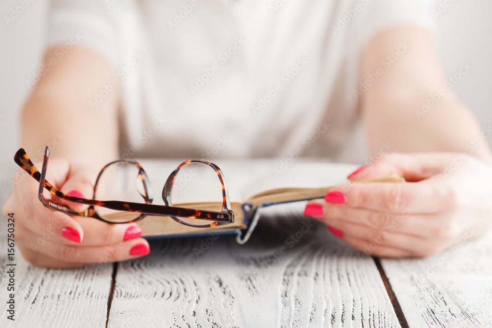 woman reading a book and in her hand she holds a pair of eyeglasses woman reading a book and in her hand she holds a pair of eyeglasses