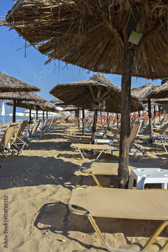 Beautiful Ionian sandy resort beach in Greece with sunbeds and straw sunshades  umbrellas. Vacation destination. Public beach