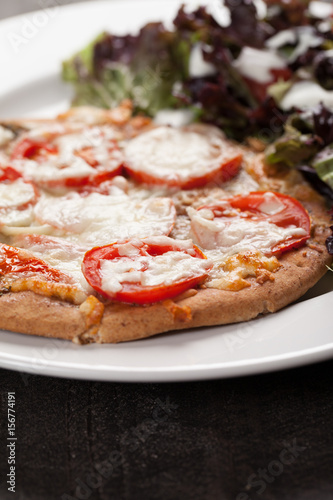  Homemade pizza with marinara sauce topped with parmesan cheese and sliced tomatoes with a side salad macro shot 