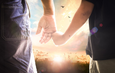 Close up of a father and son holding hands and walking together on a grass field at sunset, international father's day, family love, support and future generation concept