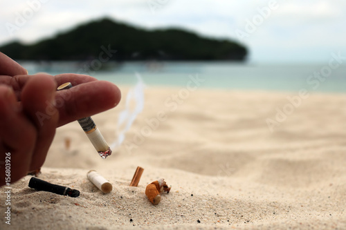 Hand smoking cigarette and ashtray on the beach.  