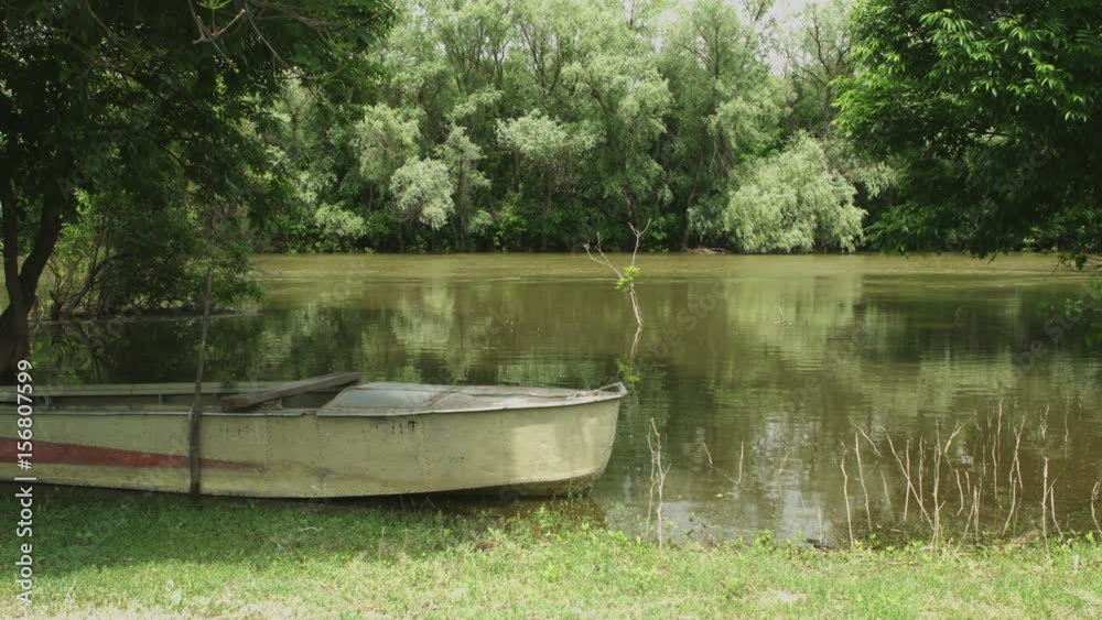 Old fishing boat on the shore of calm river surrounded by trees Old fishing boat on the shore of calm river surrounded by trees