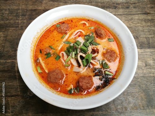 Healthy eating meal Thai hot and spicy Tomyum noodle with boiled fish and shrimp ball and herb on white bowl in restaurant,Thai local noodle soup recipe, Top view foreground focused blur background
