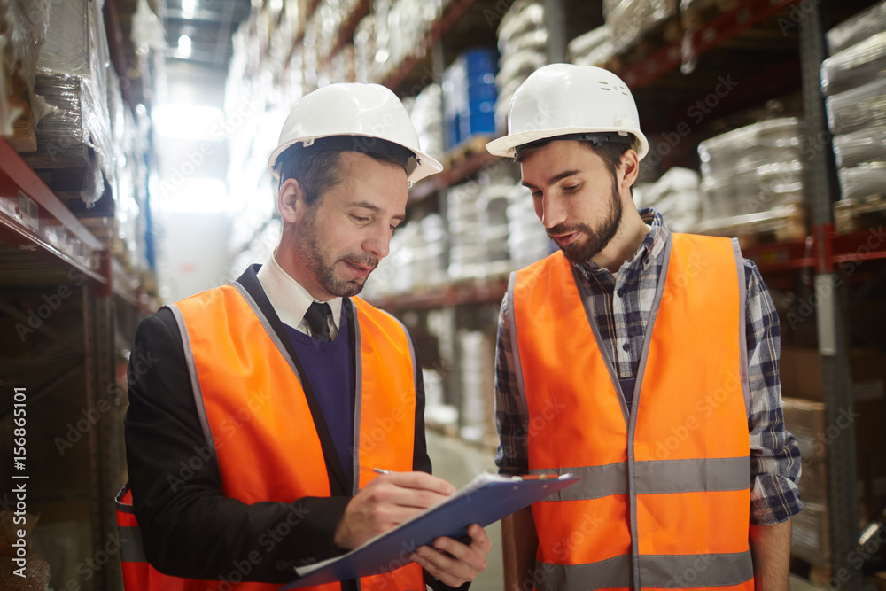 Two warehouse workers filling in document Two warehouse workers filling in document