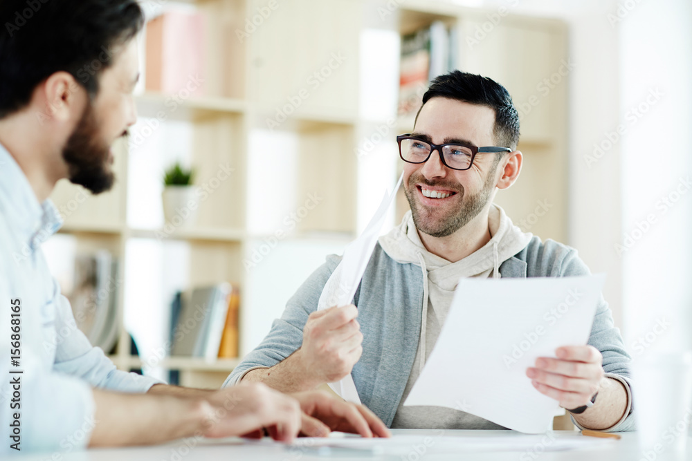 Portrait of modern man wearing casual clothes working with documents in office meeting, smiling cheerfully and looking at colleague Portrait of modern man wearing casual clothes working with documents in office meeting, smiling cheerfully and looking at colleague