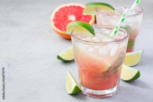 Cold pink cocktail with fresh grapefruit, lime and ice cubes on concrete background, paloma, copy space