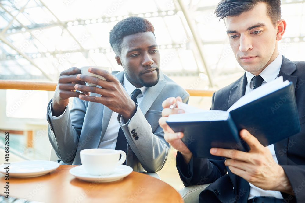 Businessmen reading notes in notebook while having tea Businessmen reading notes in notebook while having tea
