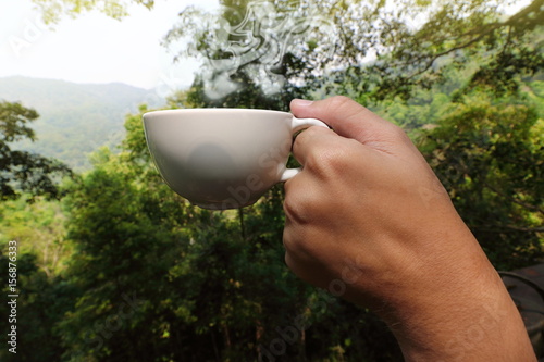Close up hands of young tourist holding coffee cup in beautiful morning nature background.