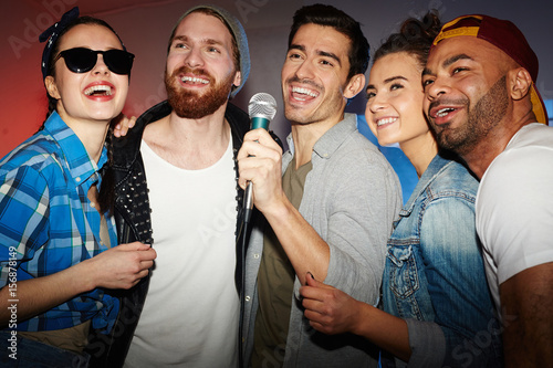 Group of buddies singing karaoke in club