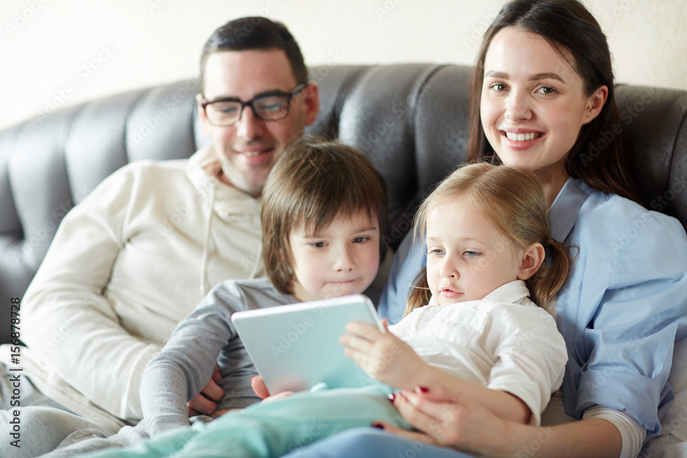 Young couple and their kids spending leisure with touchpad Young couple and their kids spending leisure with touchpad