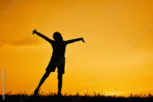 Silhouette of happy girl standing on grass field and sky sunset