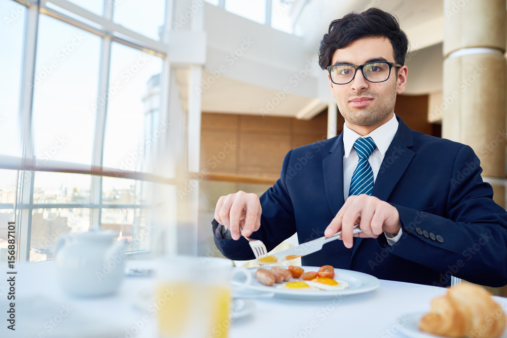 Hungry businessman cutting snack while having breakfast Hungry businessman cutting snack while having breakfast