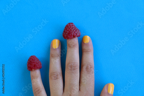 Raspberries on fingers. Teal background. 