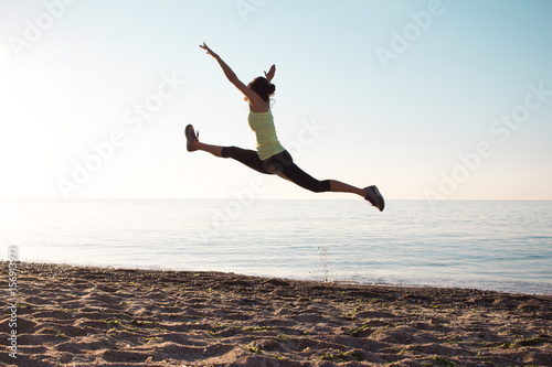 young professional gymnast woman dance on the beach, training exercises with cool junps, sunrise in sea or ocean background 